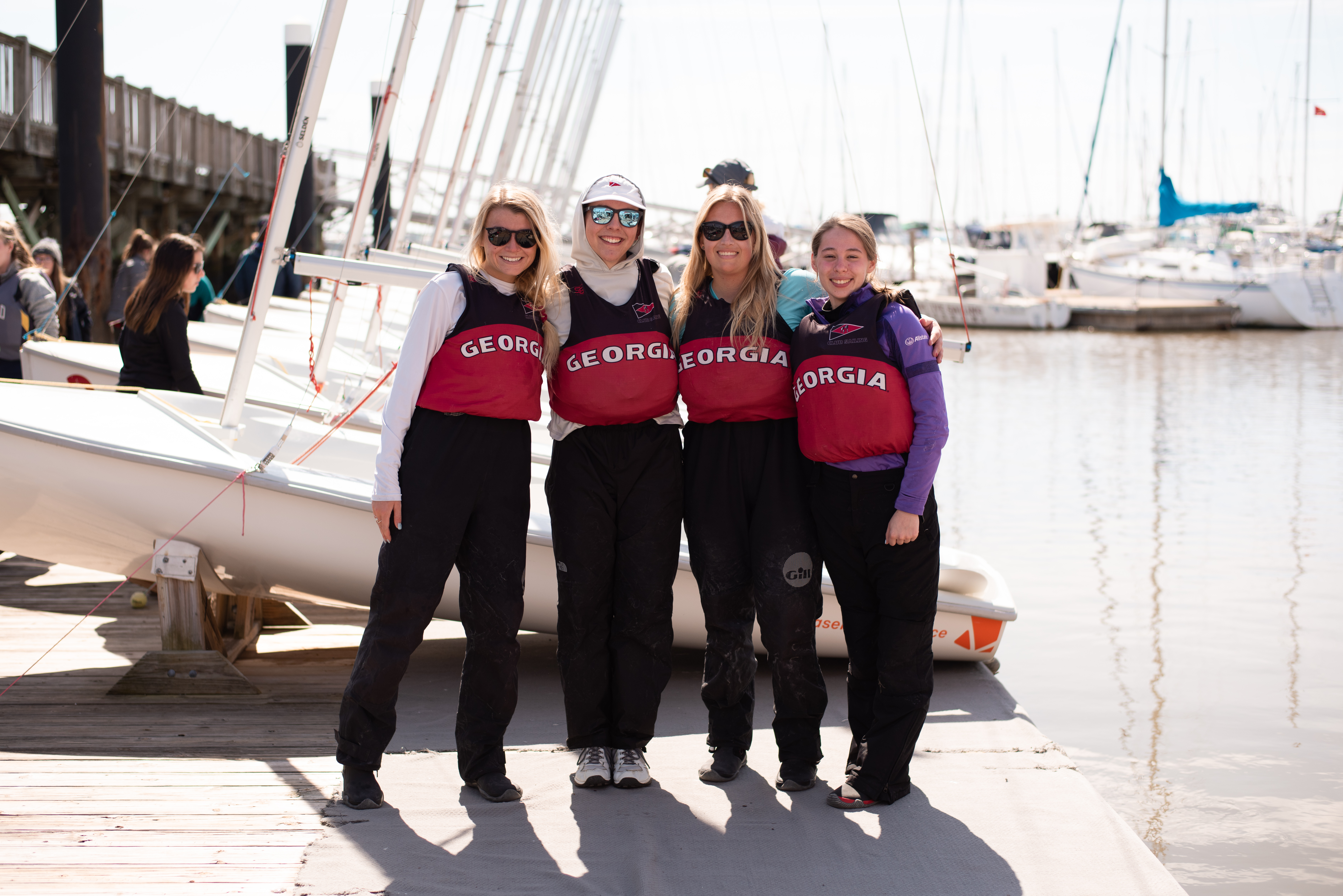 College sailors standing beside boats at a marina